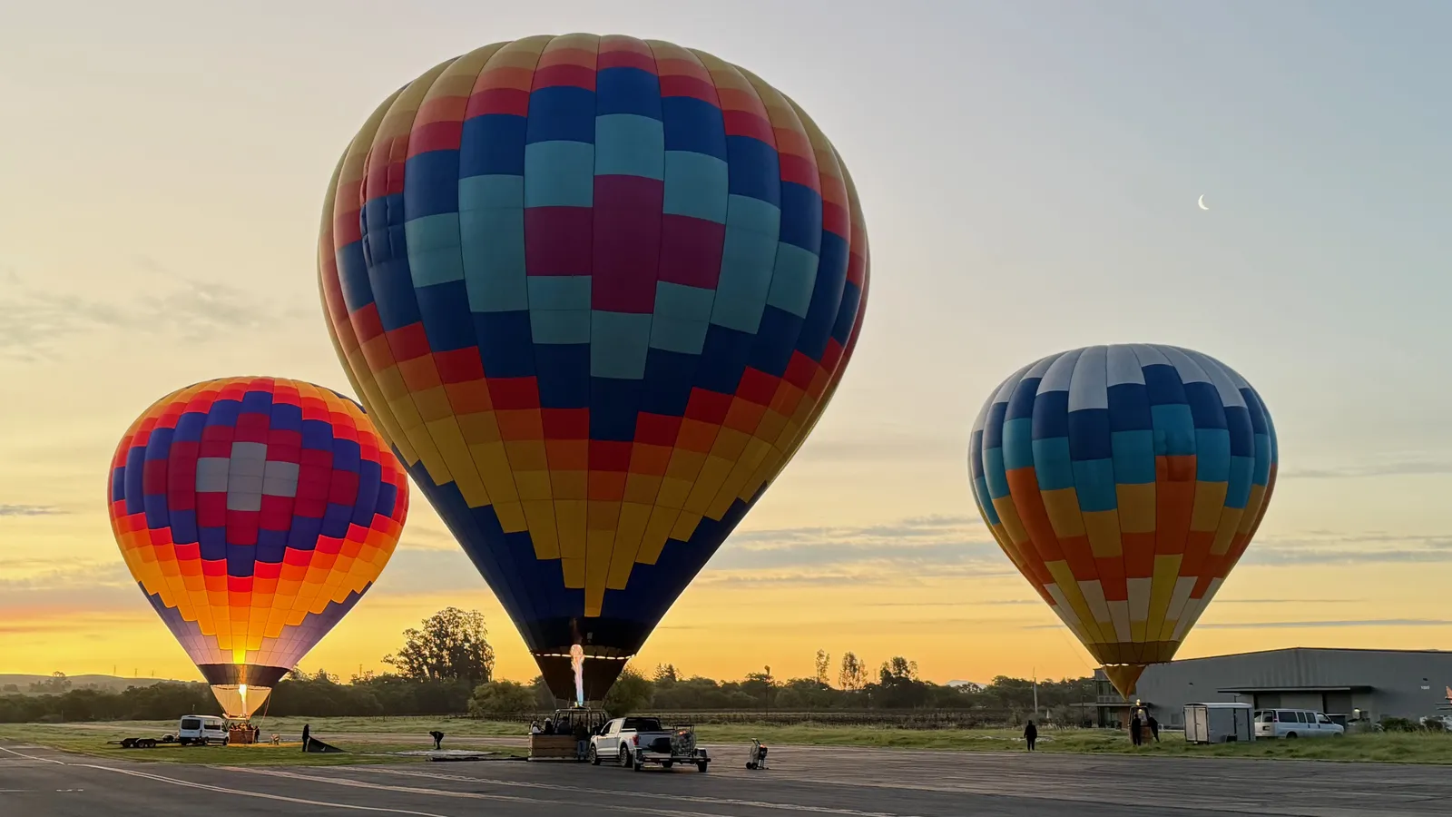 Three hot air balloons and ground crew preparing at first light