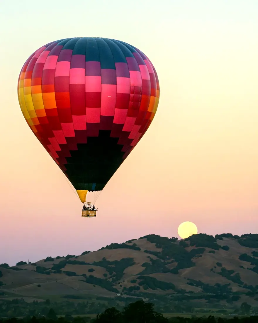 Hot air balloon at dawn with a full moon setting over Sonoma hills